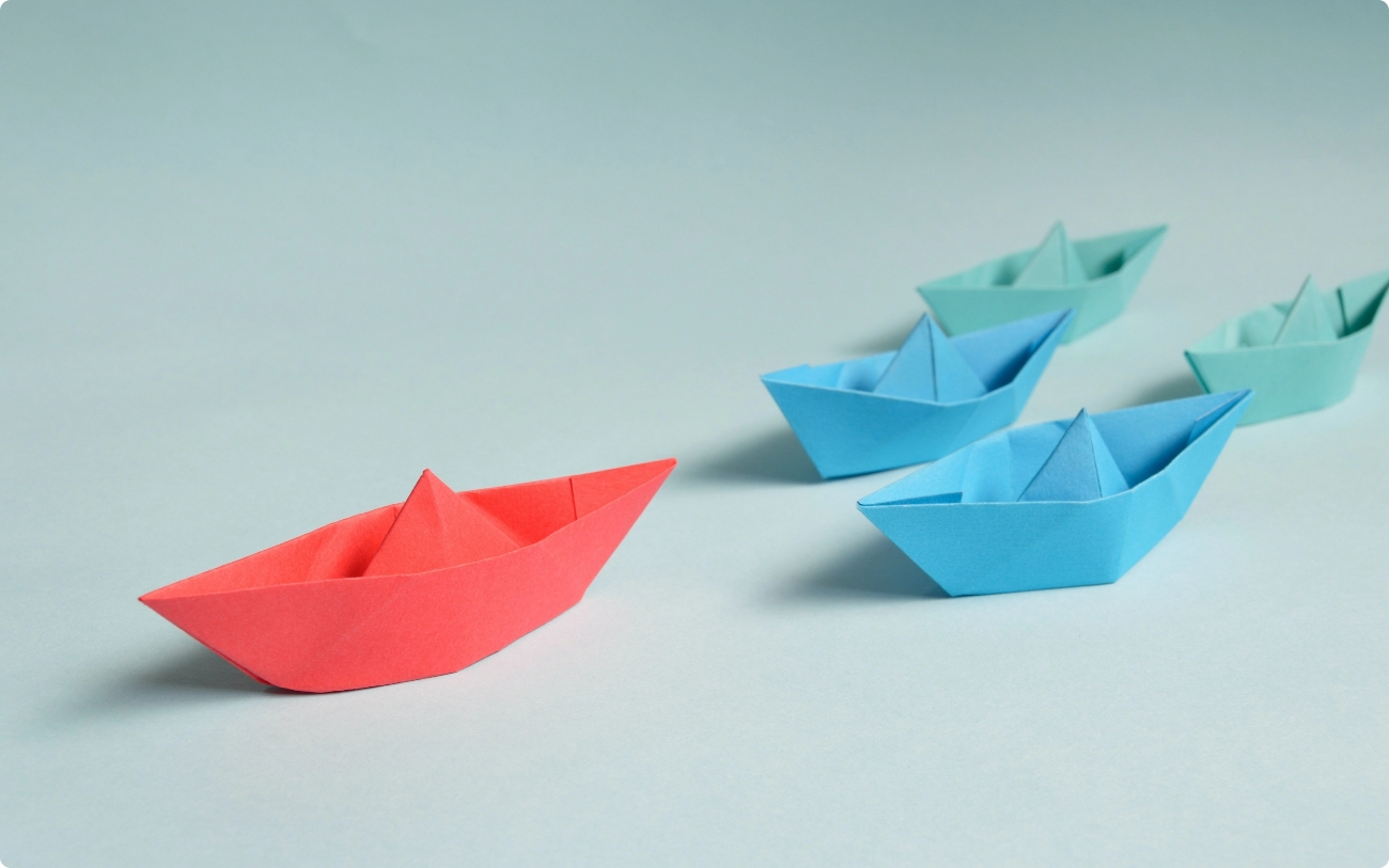 imagen de barcos de papel en diferentes colores siguiendo al líder